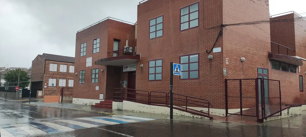 The same Consultorio Local seen from the street corner: brick building, a zebra crossing and wet asphalt after the rain.